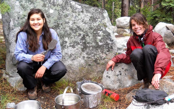 two young people use camping stoves to prepare food on on outward bound course